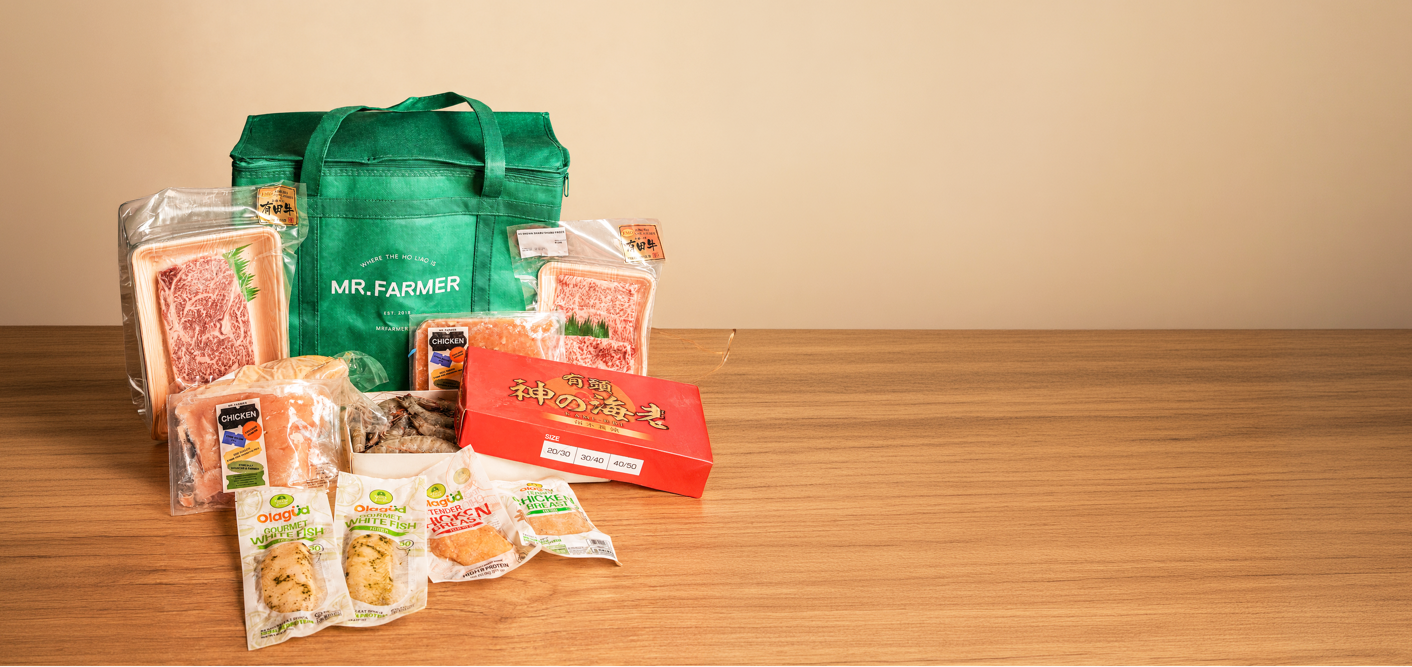 A green reusable shopping bag with the brand name 'MR. FARMER' printed on it, surrounded by assorted packaged grocery items including breads, snacks, and packaged goods, arranged on a wooden tabletop against a plain beige wall.